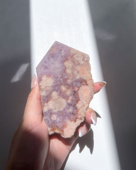Hand holding Naomi Flower Agate slab showing peachy floral formations and lavender core