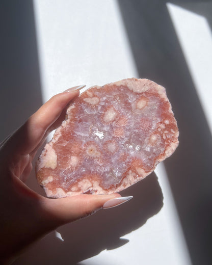 Juliette Flower Agate freeform held under sunlight, showing pink crystal blooms and sparkling druzy center