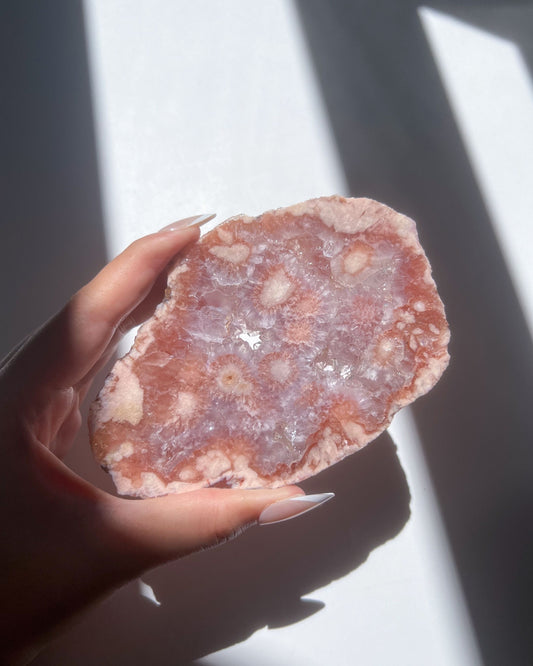 Juliette Flower Agate freeform held under sunlight, showing pink crystal blooms and sparkling druzy center
