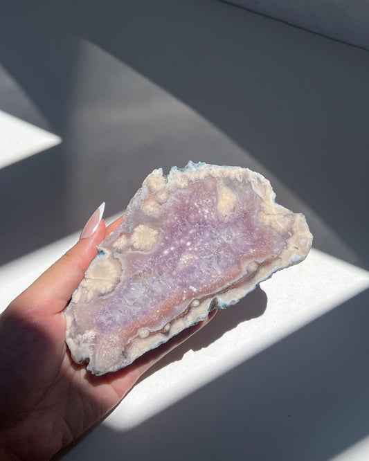 Eleanor Flower Agate slice held in hand under sunlight, showing lilac and cream crystal blooms