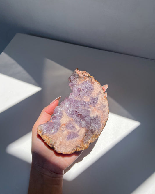 Hand holding lilac Flower Agate moon slab with peach-toned backing in sunlight