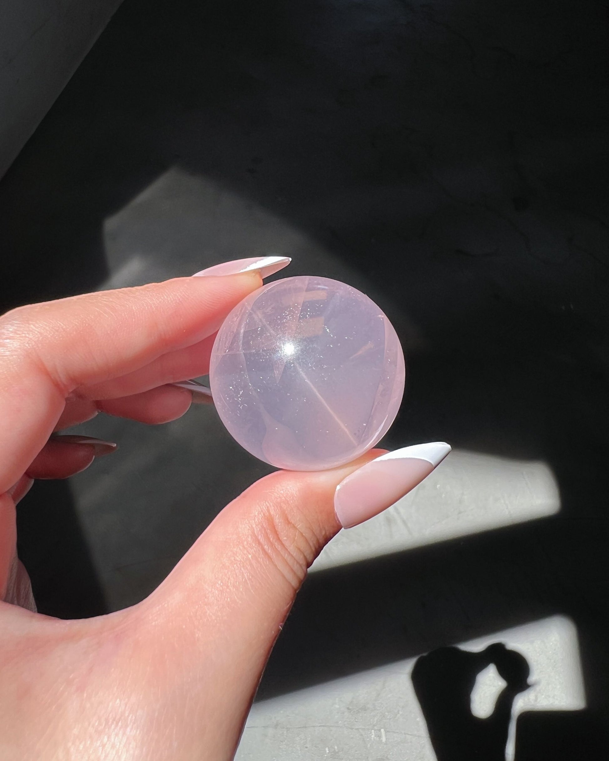 Girasol Rose Quartz sphere held under direct sunlight, showing glowing internal veils and a soft internal starburst reflection, set against a dark background.