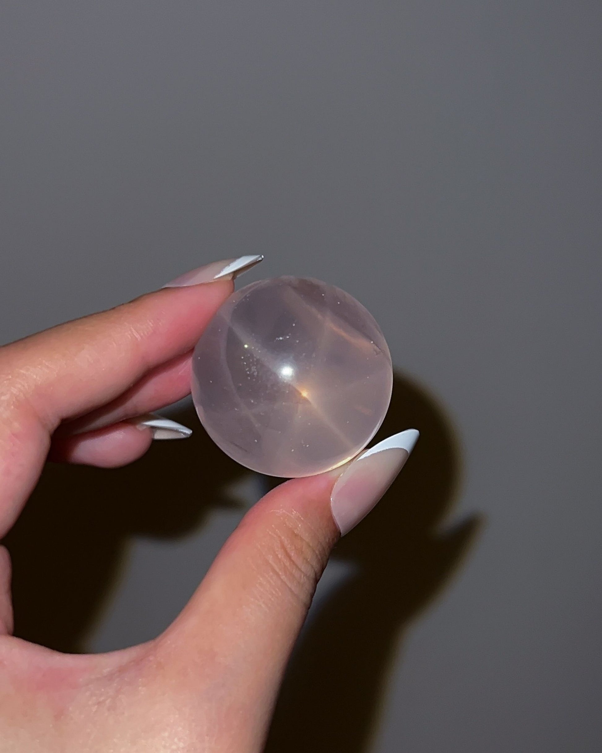 Girasol Rose Quartz sphere viewed under flash lighting, revealing strong inner clarity and a glowing star effect across the translucent surface
