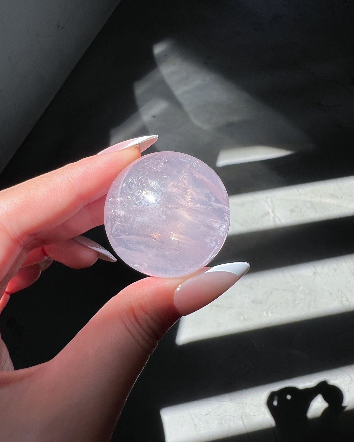 Close-up of translucent Girasol Rose Quartz crystal ball with silky veils and internal shimmer, illuminated by bright morning light.