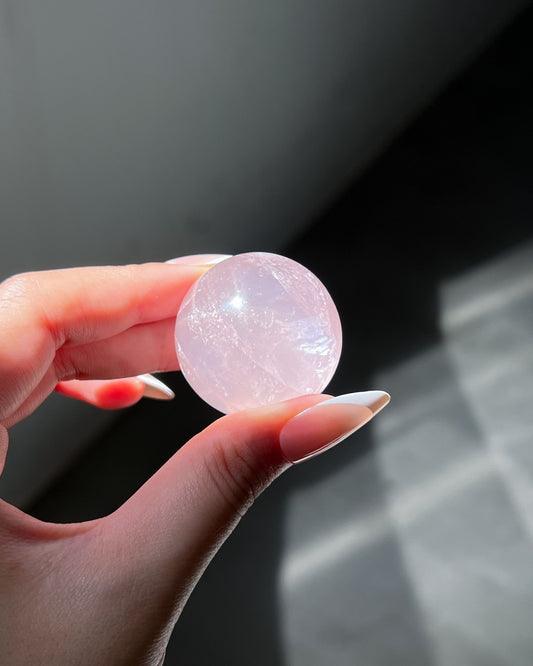 Translucent Girasol Rose Quartz sphere glowing in sunlight, revealing vivid internal shimmer and intricate cloudy inclusions.