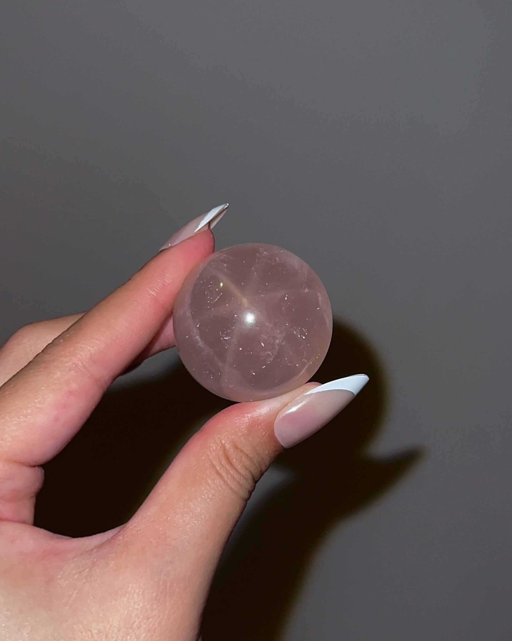 Girasol Rose Quartz gemstone sphere photographed with flash, showing a prominent starburst effect and soft pink translucency.