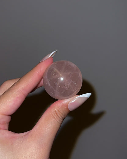 Girasol Rose Quartz gemstone sphere photographed with flash, showing a prominent starburst effect and soft pink translucency.