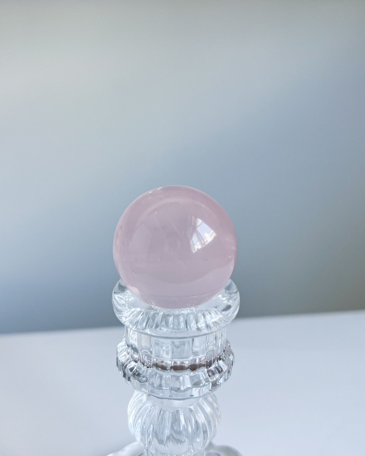 Polished Girasol Rose Quartz sphere displayed on an ornate glass stand, with a silky pink finish and soft natural lighting.