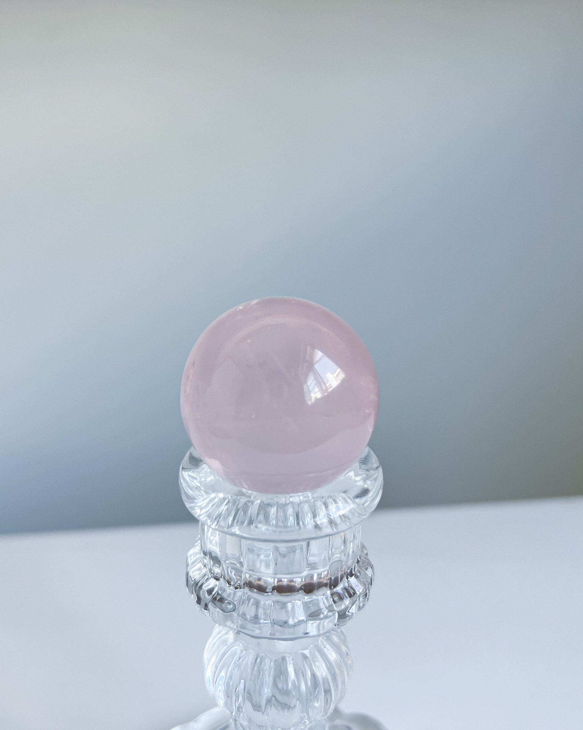 Polished Girasol Rose Quartz sphere displayed on an ornate glass stand, with a silky pink finish and soft natural lighting.