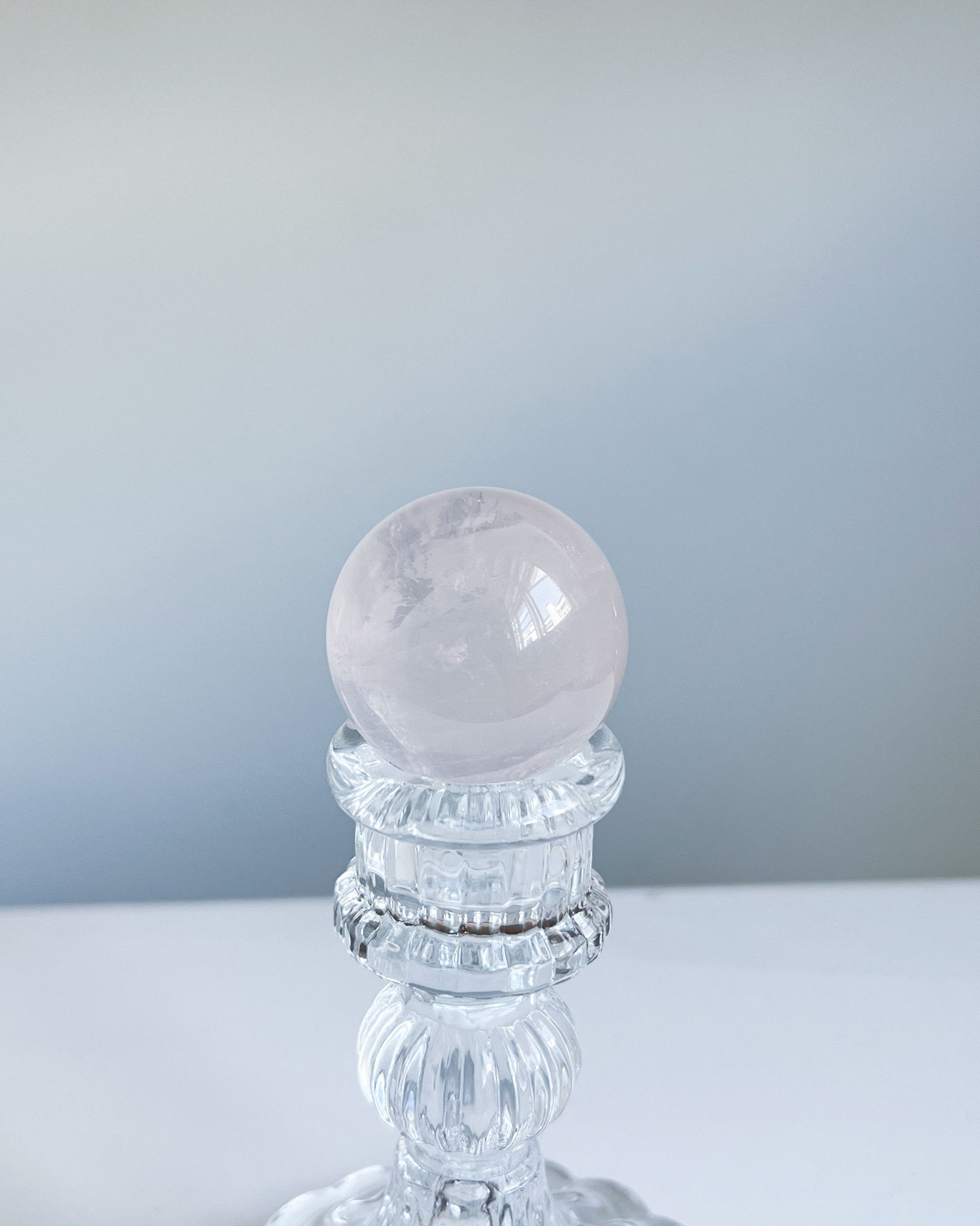 Girasol Rose Quartz sphere held above a clear pedestal, featuring a glassy surface with soft blush tone and faint internal mist.