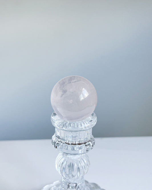 Girasol Rose Quartz sphere held above a clear pedestal, featuring a glassy surface with soft blush tone and faint internal mist.