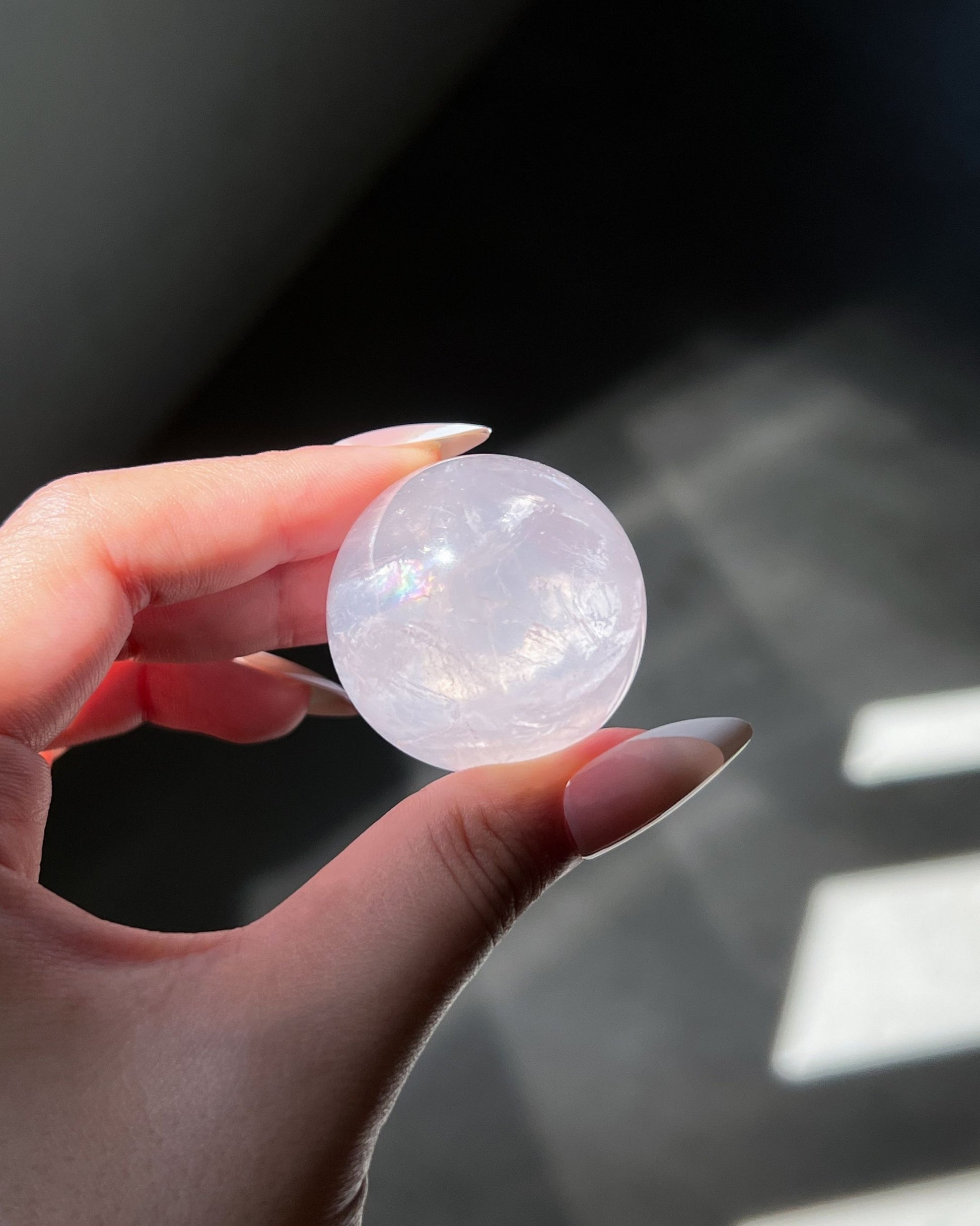 Girasol Rose Quartz crystal sphere under flash, showing internal shimmer and distinct rainbow reflections within its soft pink clarity.