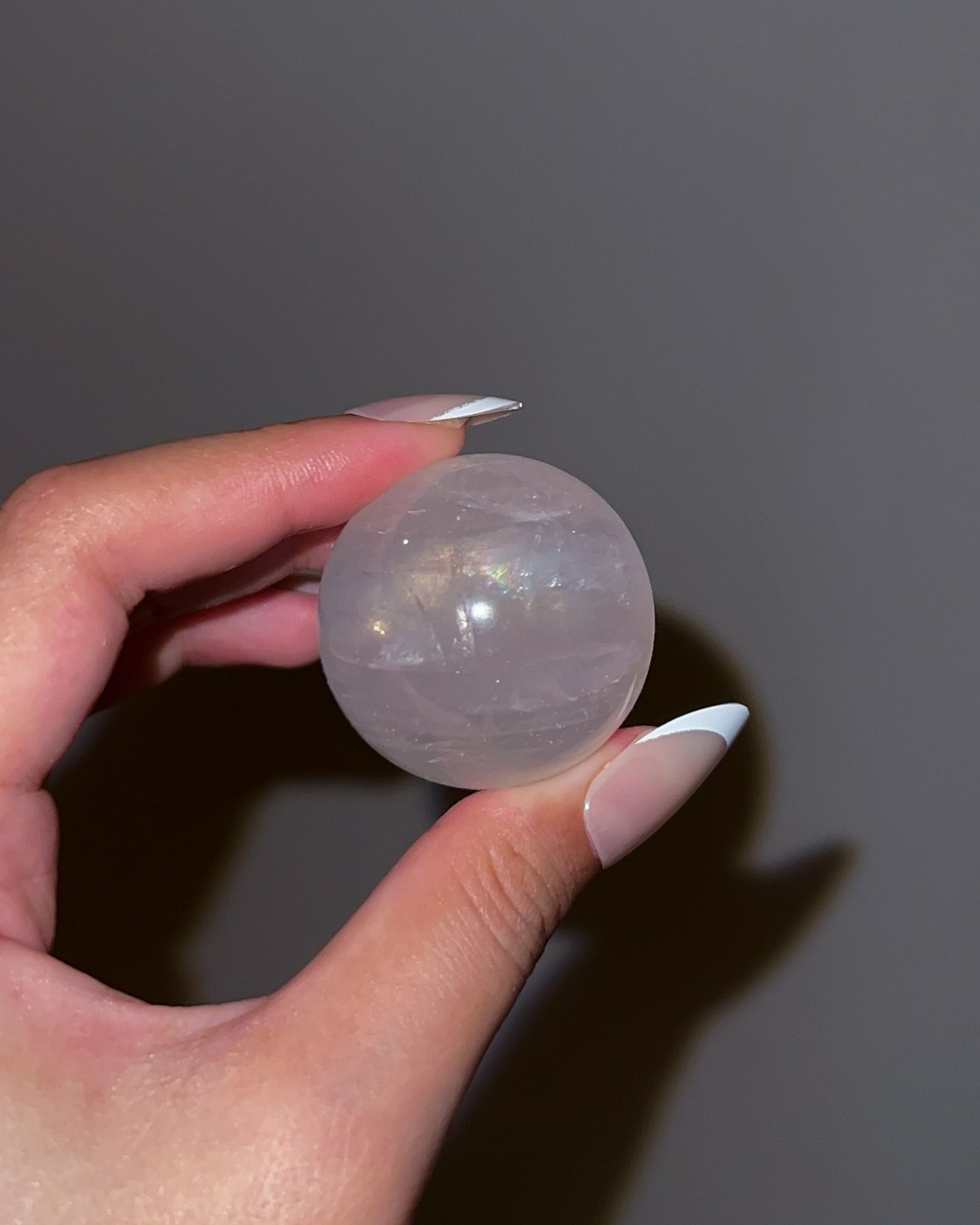 Soft pink Girasol Rose Quartz gemstone sphere with silky internal swirls, displayed above an ornate ribbed pedestal in natural light.