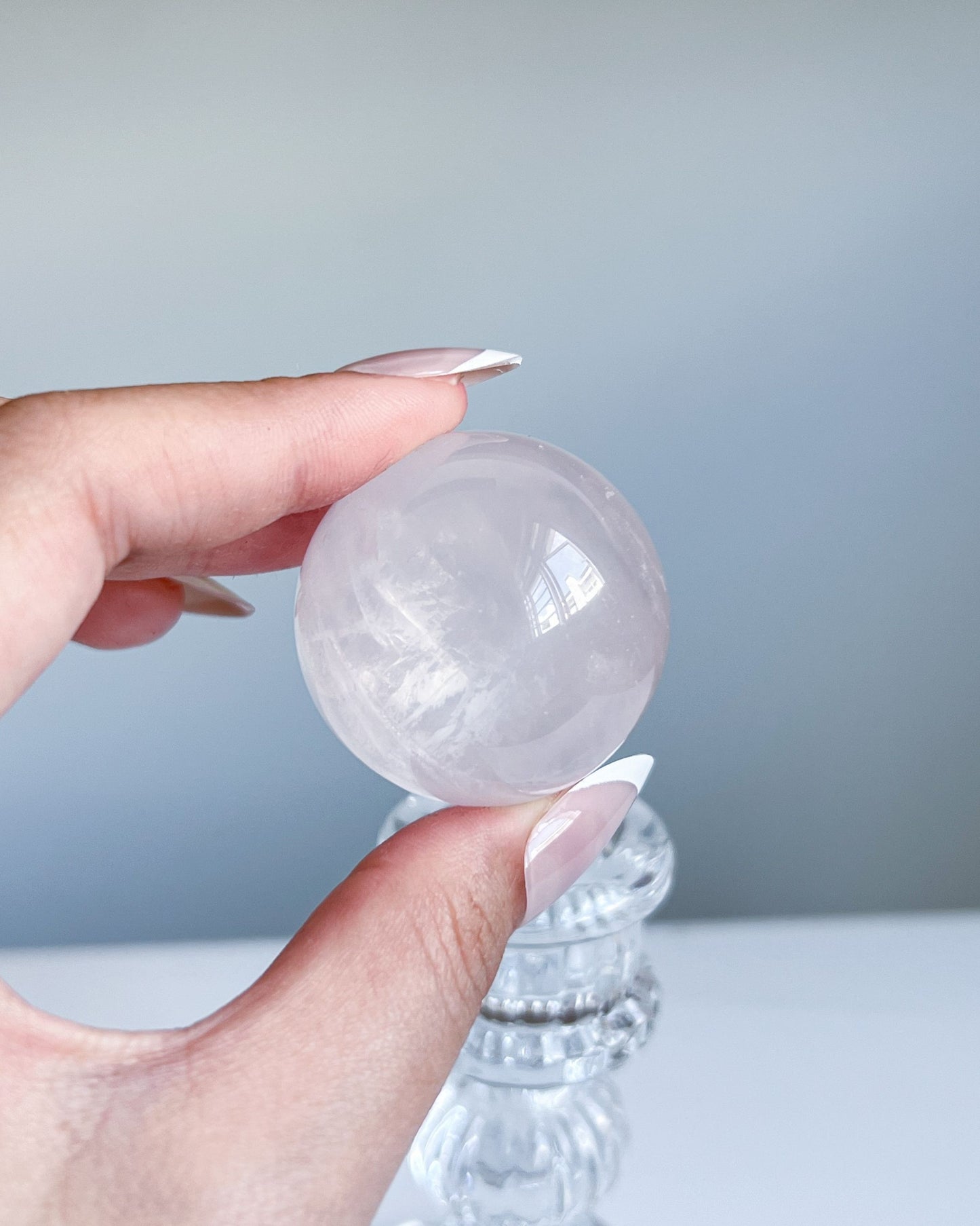 Girasol Rose Quartz sphere held at eye level above a glass pedestal, showing inner cloudiness and high polish under soft daylight.