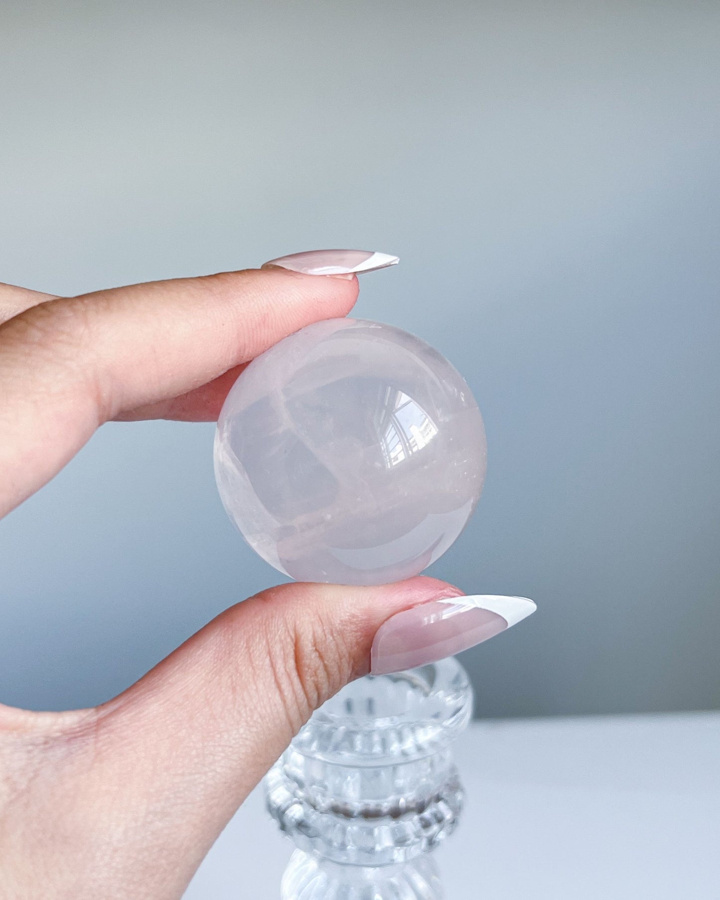 Polished Girasol Rose Quartz crystal resting on a clear vintage-style stand, with soft grey background and subtle pink transparency.