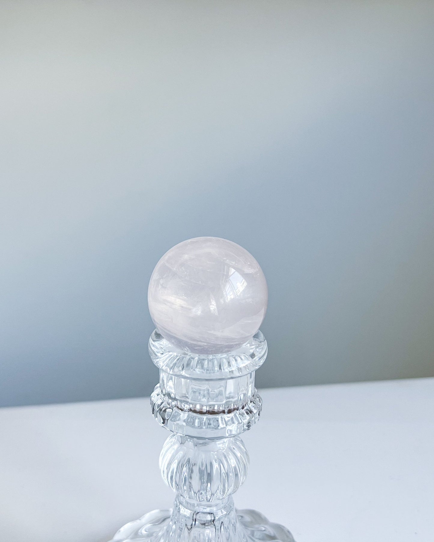 Blush-toned Girasol Rose Quartz sphere placed on a glass pedestal, showing delicate natural veining and a soft luminous surface.