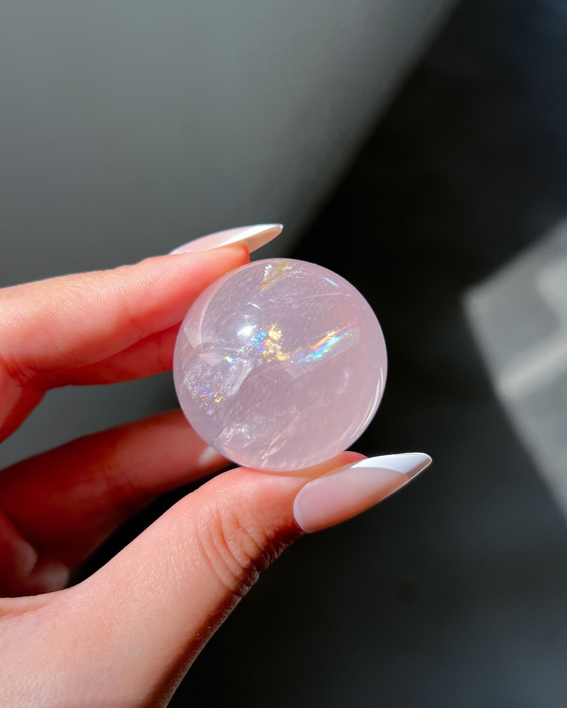 Girasol rose quartz sphere illuminated by sunlight, highlighting vivid rainbows and inner fissures in a warm blush tone.