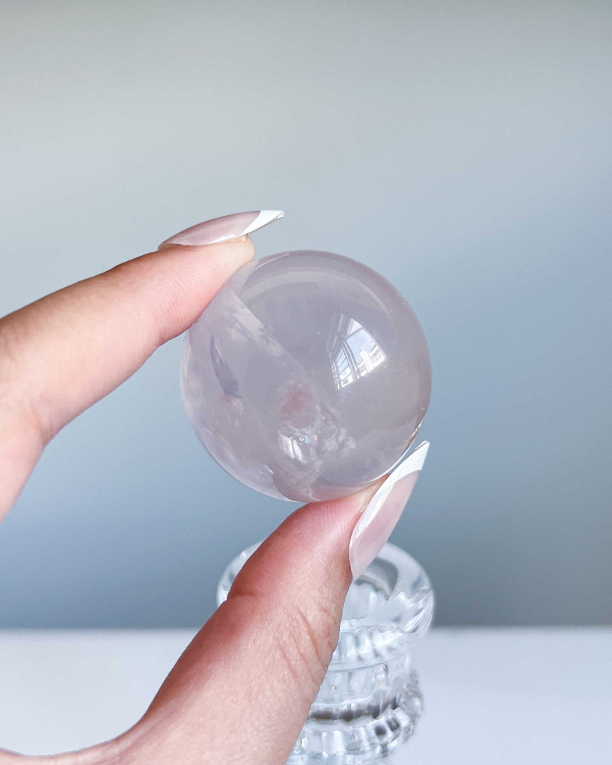 Close-up of girasol rose quartz sphere held between fingers, natural daylight revealing cloudy inclusions and soft reflectivity.