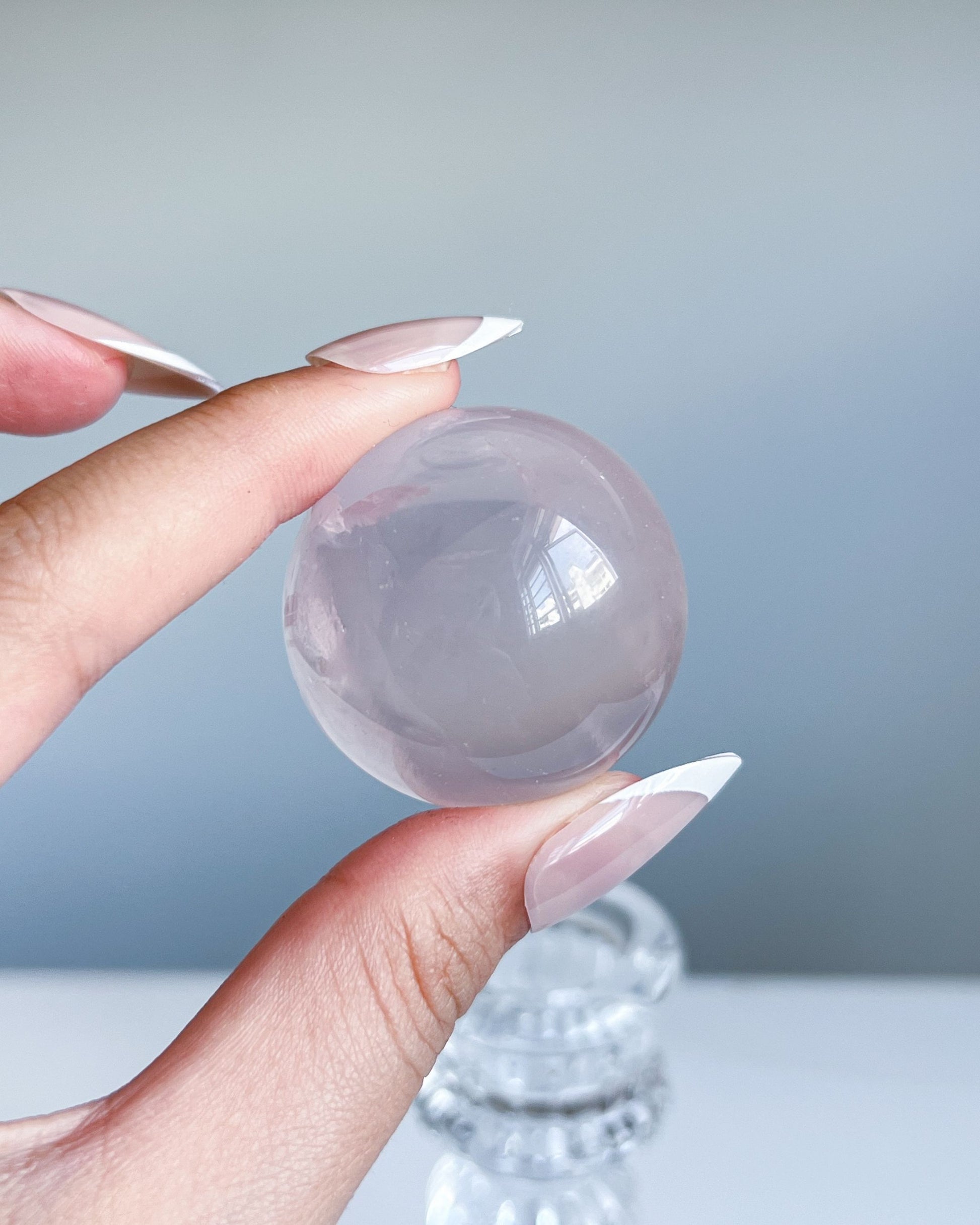 Light pink girasol rose quartz sphere held against a grey background, with soft inner whirls and glassy finish.