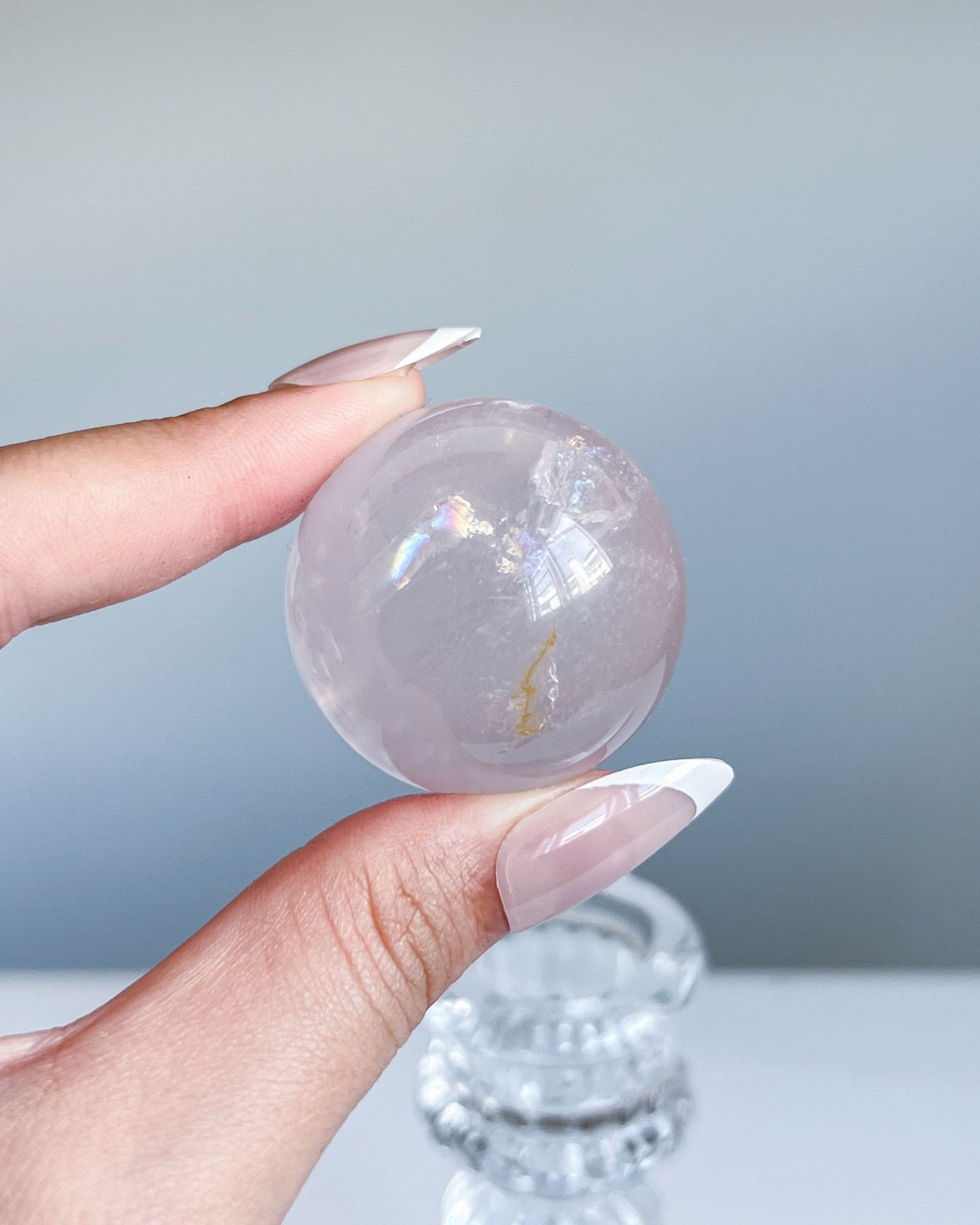 Girasol rose quartz sphere held delicately, showing ethereal rainbows and a golden healer inclusion under clear daylight.