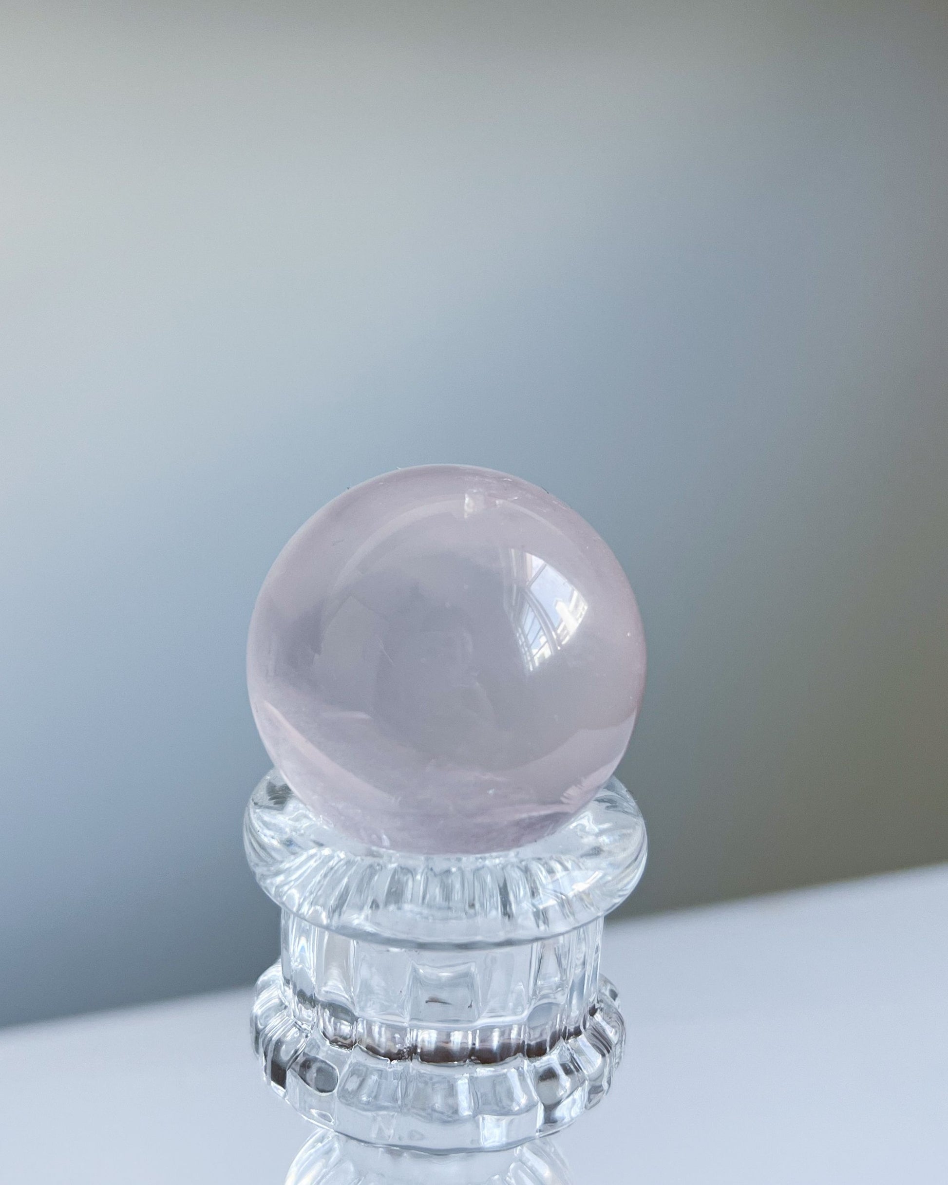 Dreamy girasol rose quartz sphere on a crystal pedestal, captured in gentle ambient light with a luminous, misty core.