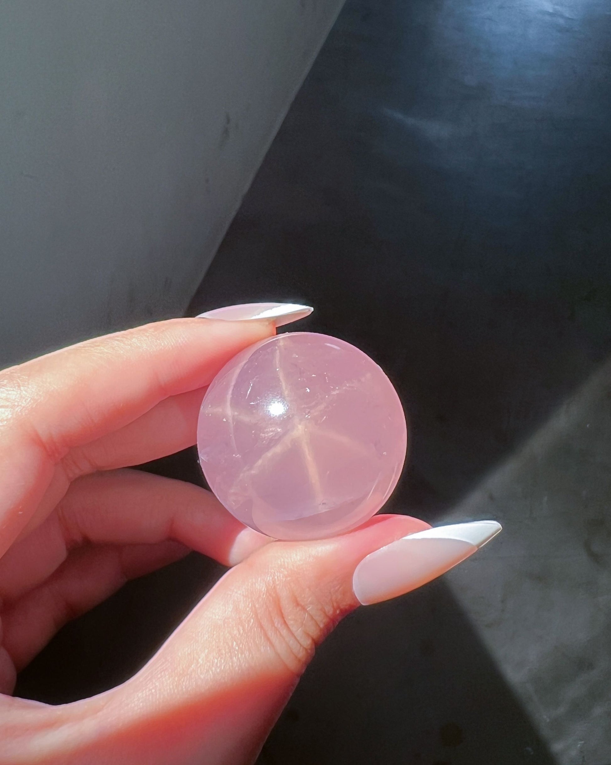 Girasol Rose Quartz Sphere H held under direct sunlight, revealing a visible starburst asterism within the crystal