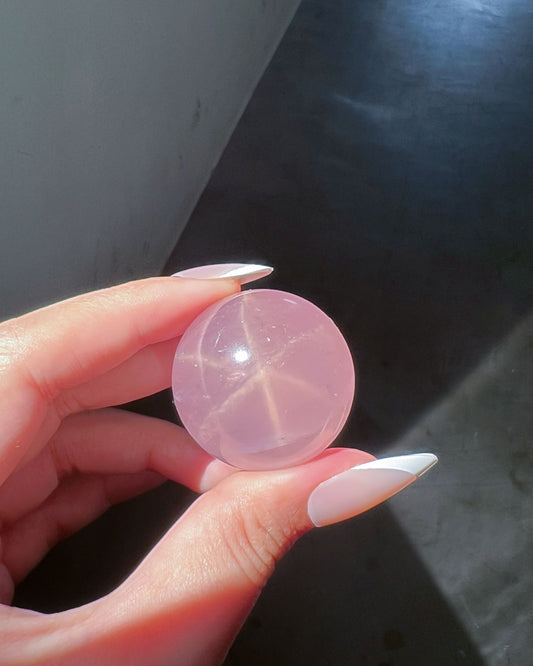 Girasol Rose Quartz Sphere H held under direct sunlight, revealing a visible starburst asterism within the crystal