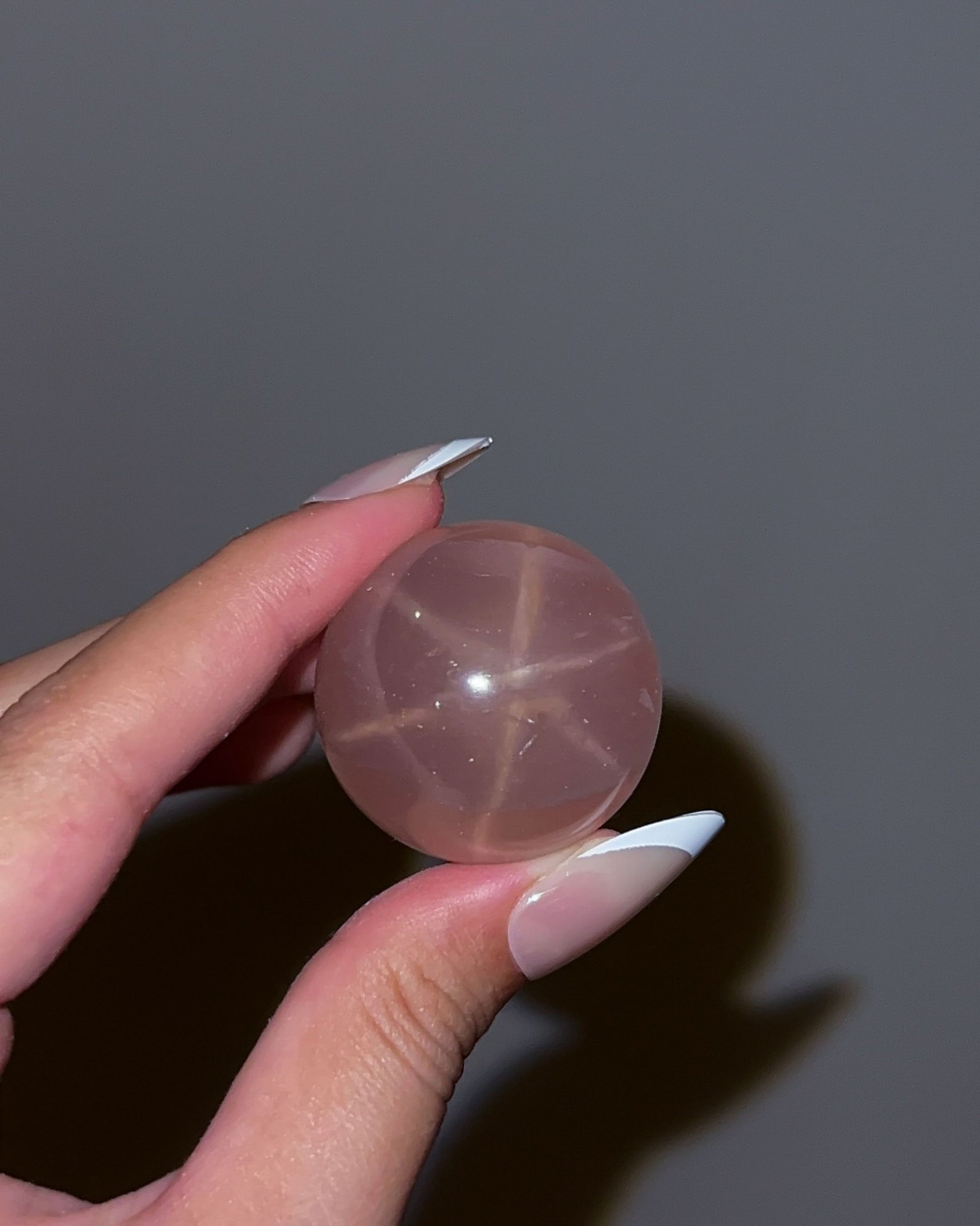 Close-up of Girasol Rose Quartz Sphere H in flash lighting, highlighting the sharp star asterism and inner glow
