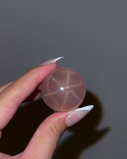 Close-up of Girasol Rose Quartz Sphere H in flash lighting, highlighting the sharp star asterism and inner glow