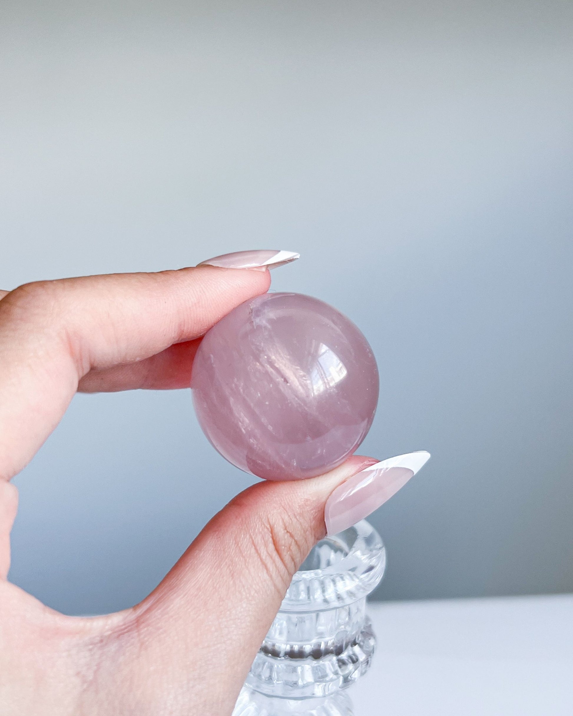 Side angle of Girasol Rose Quartz Sphere H, showing banded reflections and silky shimmer in natural light