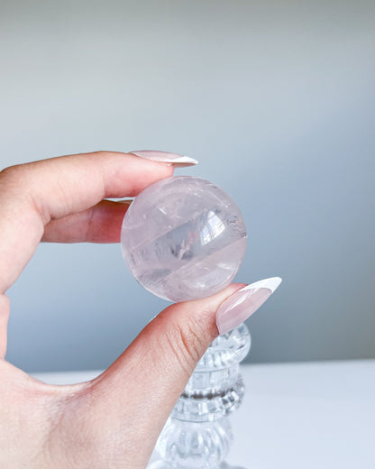 Girasol Rose Quartz Sphere I held above pedestal, revealing clean transparency and delicate internal swirls
