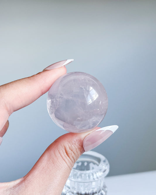 Hand holding a luminous Girasol Rose Quartz sphere with dreamy reflections against a pastel gradient background