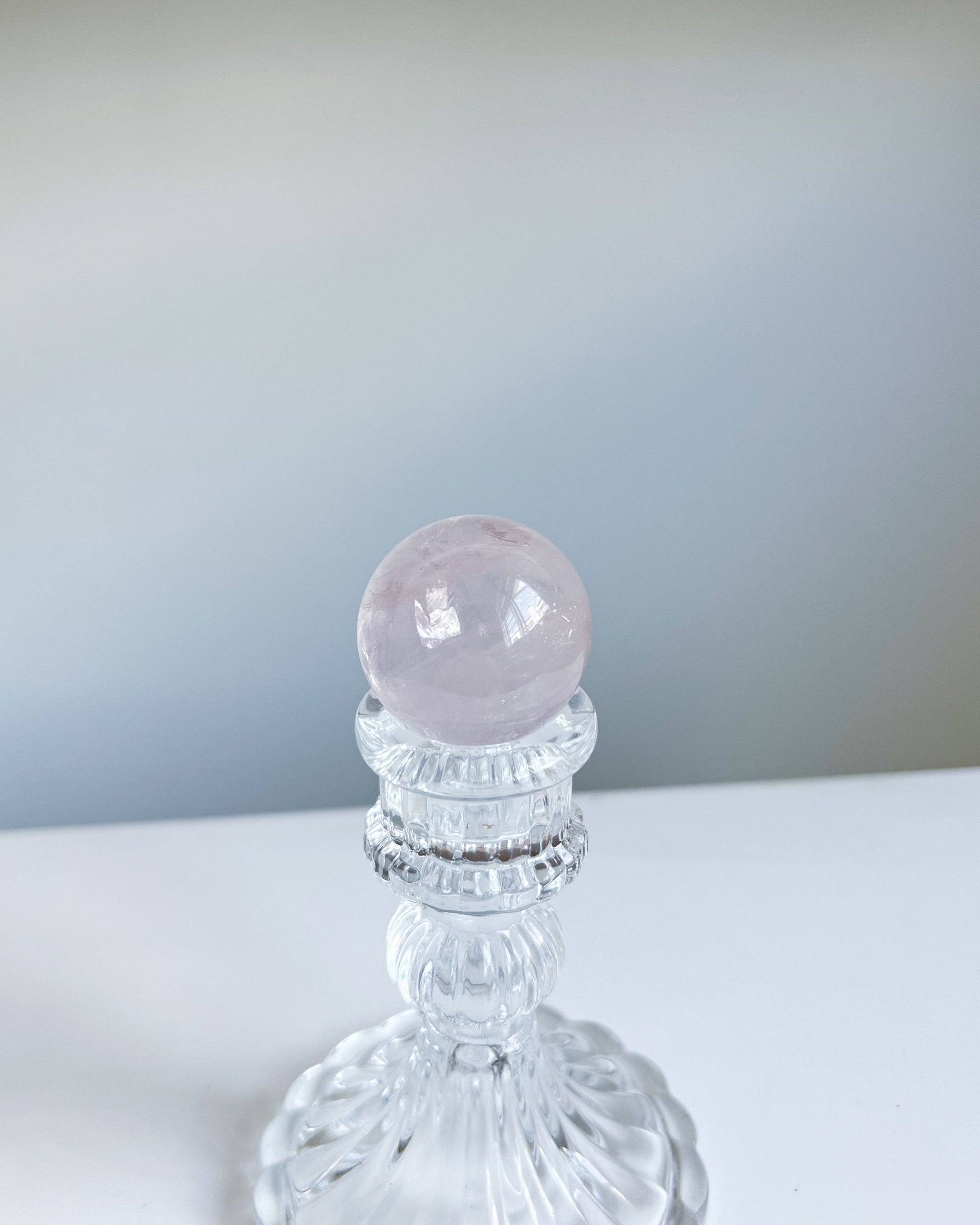 Girasol Rose Quartz sphere resting on ornate clear pedestal with soft gradients in the background