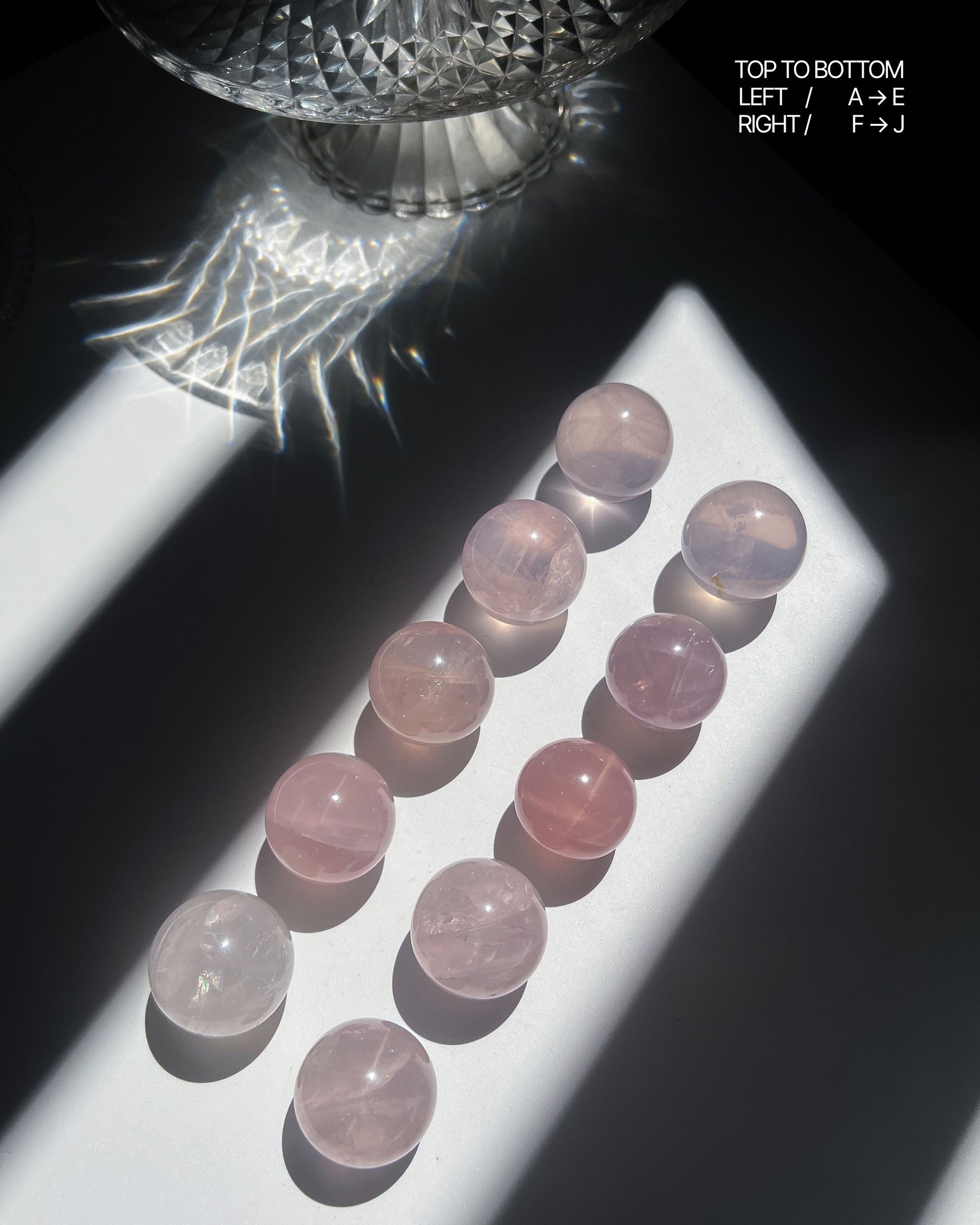 Ten Girasol Rose Quartz spheres arranged in sunlight, arranged in two vertical rows on a white tray with visible glow and soft asterism.