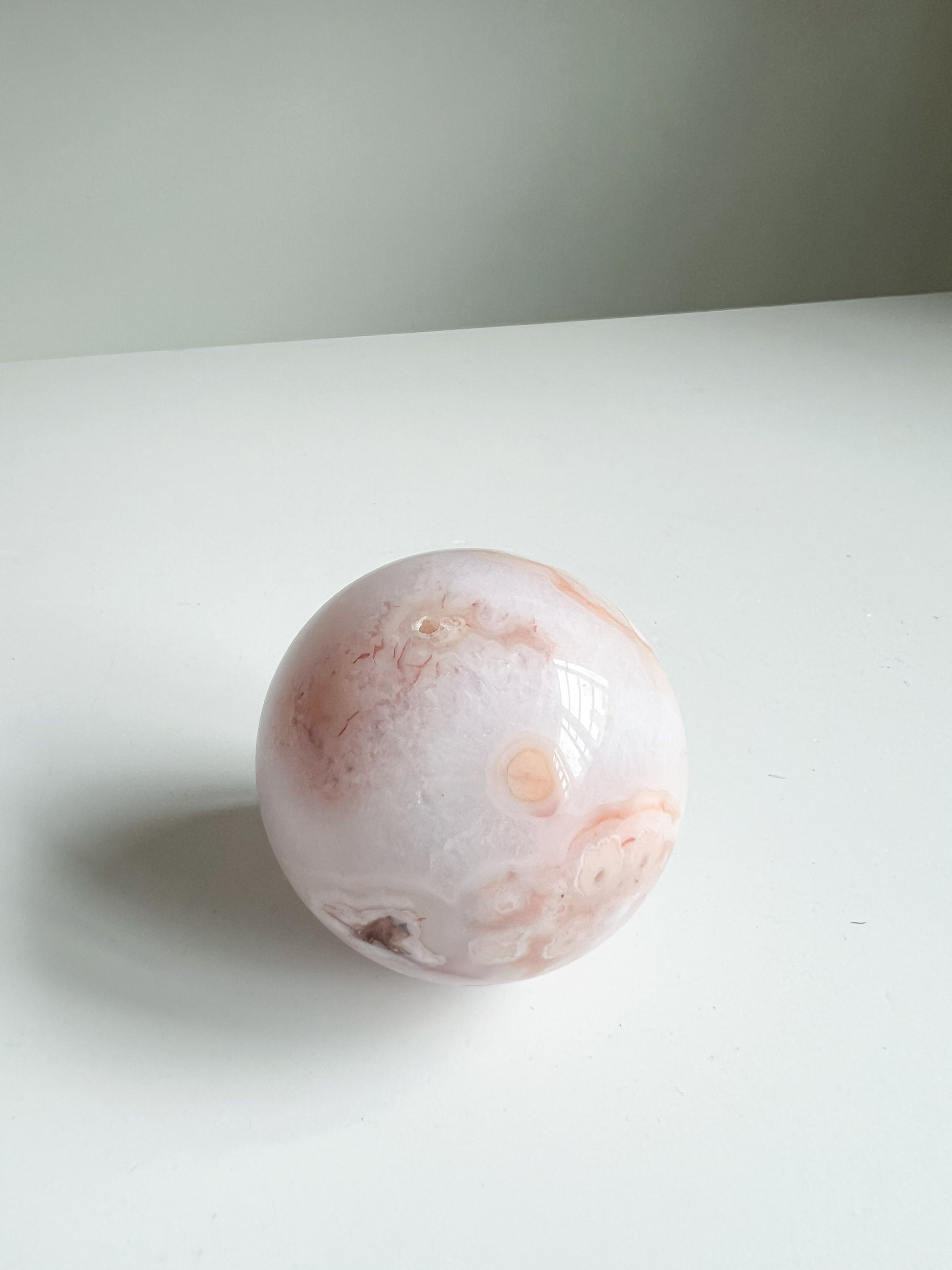 Gentle side view of a crystal sphere with soft botanical patterns and creamy undertones