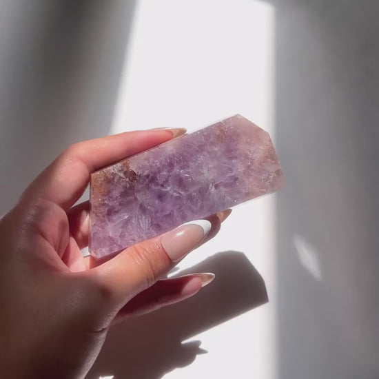 Hand holding polished purple flower agate slab under sunlight and natural daylight
