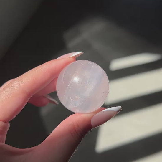 Girasol Rose Quartz sphere in hand under shifting natural light, showing orange glow, rainbows and clarity.