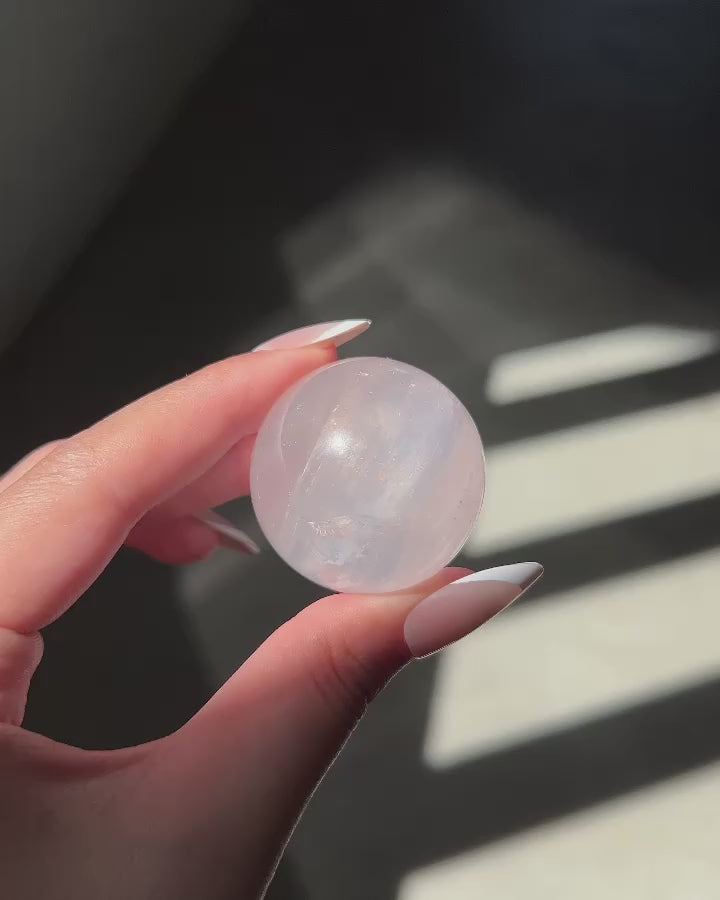 Girasol Rose Quartz sphere in hand under shifting natural light, showing orange glow, rainbows and clarity.