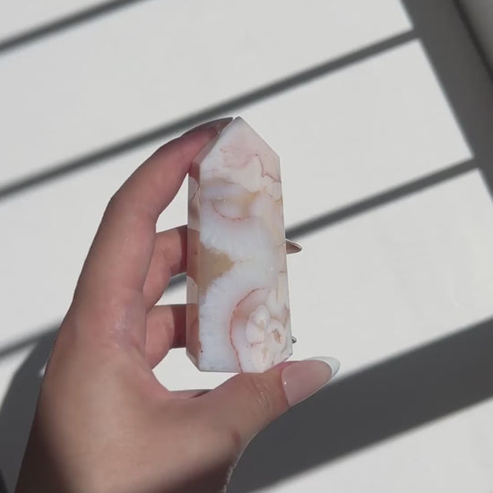 Video of hand holding a Carnelian Flower Agate tower with cream and peach tones under natural light