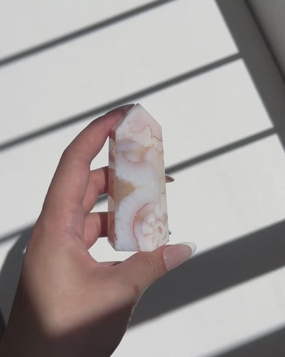 Video of hand holding a Carnelian Flower Agate tower with cream and peach tones under natural light