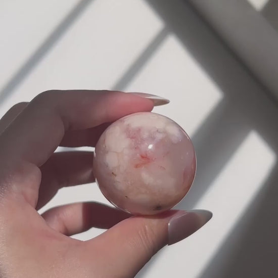 Hand holding a pale pink Carnelian Flower Agate sphere in natural sunlight with visible banding and floral plume