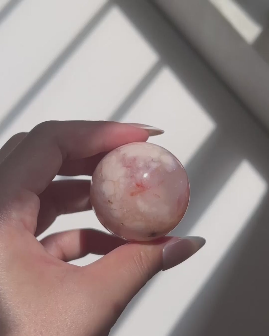 Hand holding a pale pink Carnelian Flower Agate sphere in natural sunlight with visible banding and floral plume