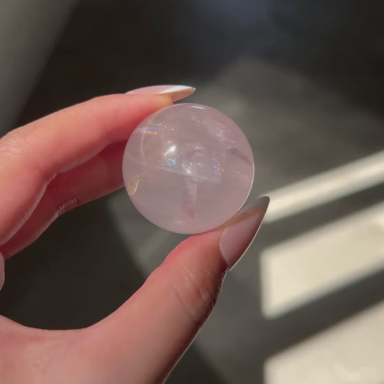 Close-up of a Girasol Rose Quartz sphere held in hand in three different lightings: sunlight, with flash and studio lighting: revealing rainbows, clarity, asterism and golden healer.