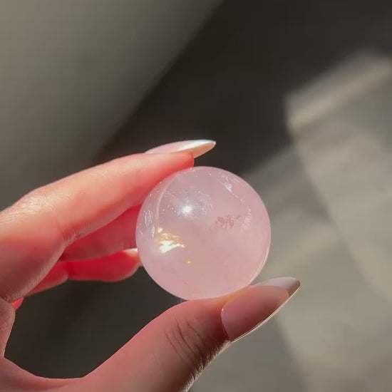Girasol Rose Quartz sphere in hand under shifting natural light, showing glowing clarity and subtle inner sparkles in motion.