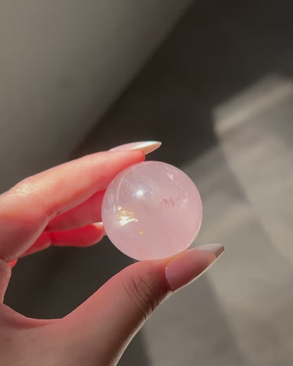 Girasol Rose Quartz sphere in hand under shifting natural light, showing glowing clarity and subtle inner sparkles in motion.
