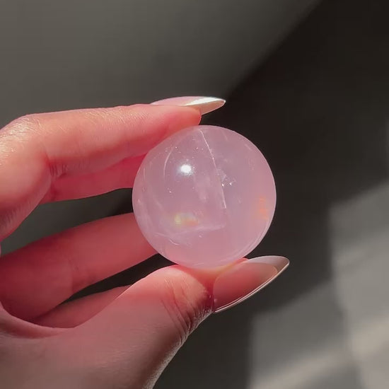 Close-up of a Girasol Rose Quartz sphere held in hand in three different lightings: sunlight, with flash and studio lighting: revealing rainbows, asterism and sparkles.