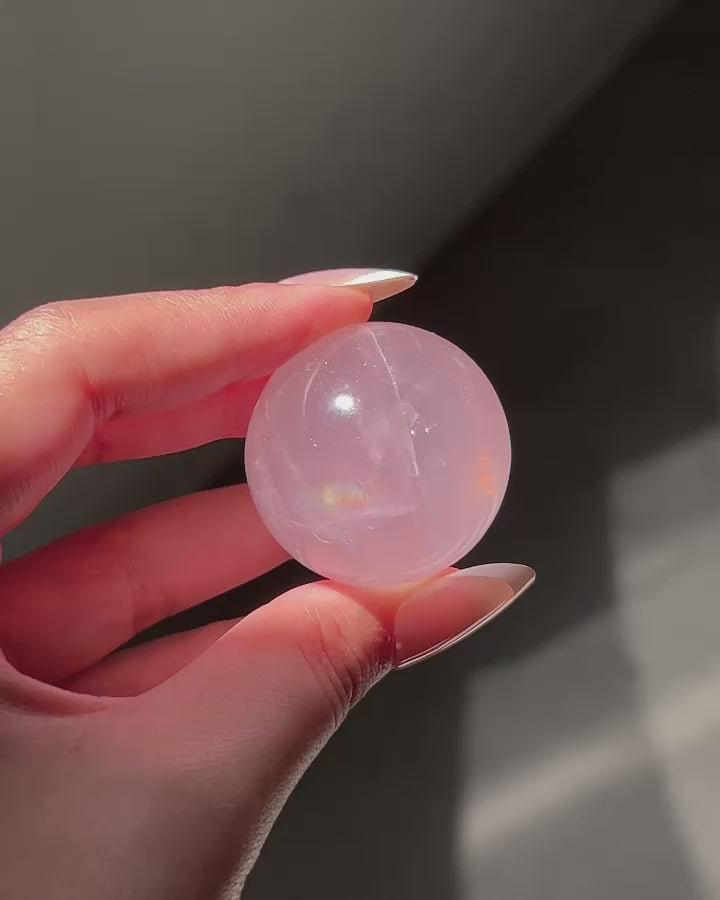 Close-up of a Girasol Rose Quartz sphere held in hand in three different lightings: sunlight, with flash and studio lighting: revealing rainbows, asterism and sparkles.