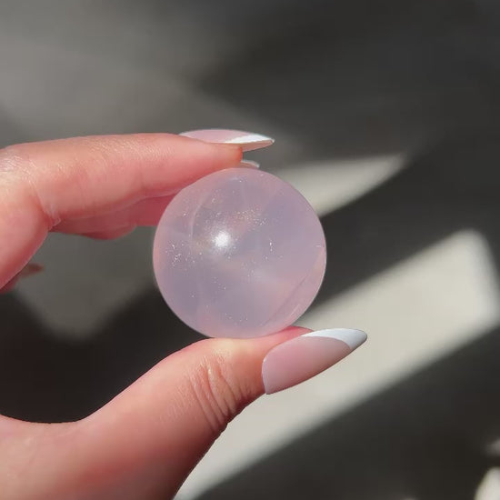 Close-up of a Girasol Rose Quartz sphere held in hand in sunlight, with flash and studio lighting: revealing delicate sparkles and inner glow.
