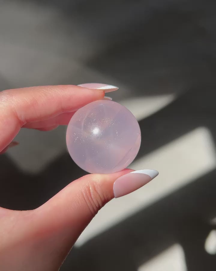 Close-up of a Girasol Rose Quartz sphere held in hand in sunlight, with flash and studio lighting: revealing delicate sparkles and inner glow.