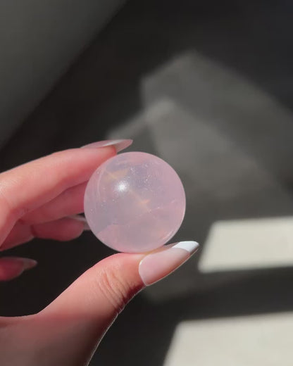 Close-up video of a Girasol Rose Quartz sphere held in hand in sunlight, with flash and studio lighting: revealing amazing asterism and ethereal glow.